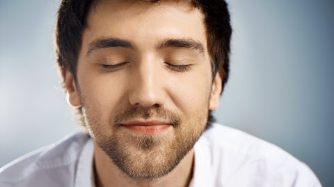 Close up portrait of relaxed elegant handsome young businessman in white shirt with closed eyes. Studio, isolated on grey background.