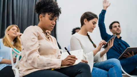 Group of young people sitting on conference together while raising their hands to ask a question. Business team meeting seminar training concept.